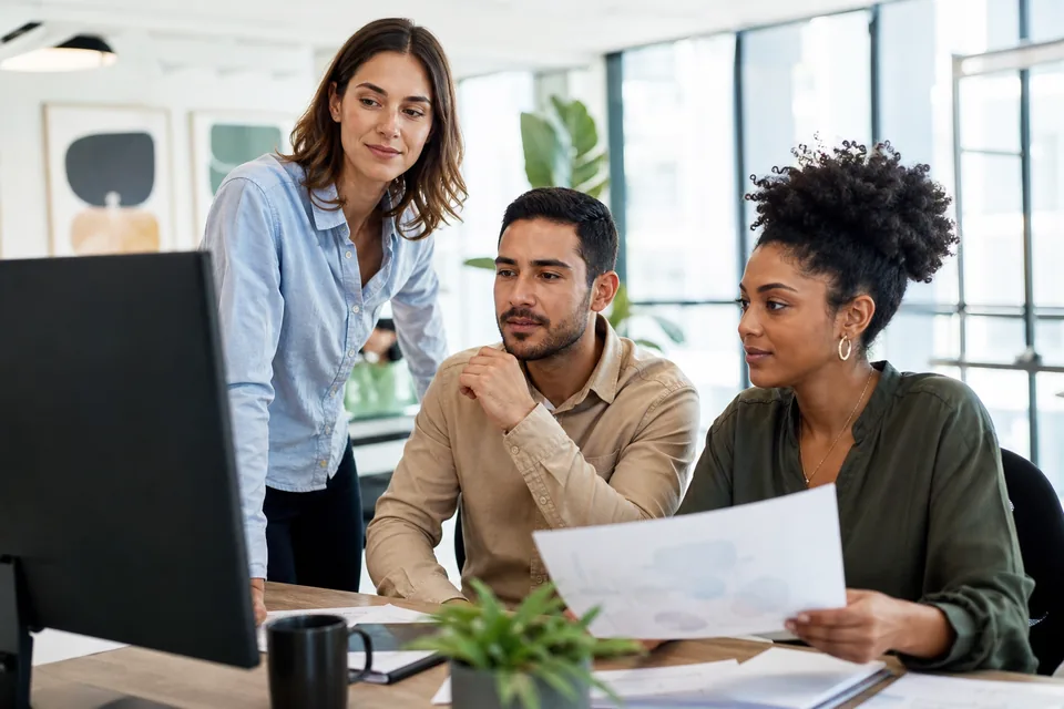 Social media team reviewing a software budget on a monitor while one member holds a printed contract